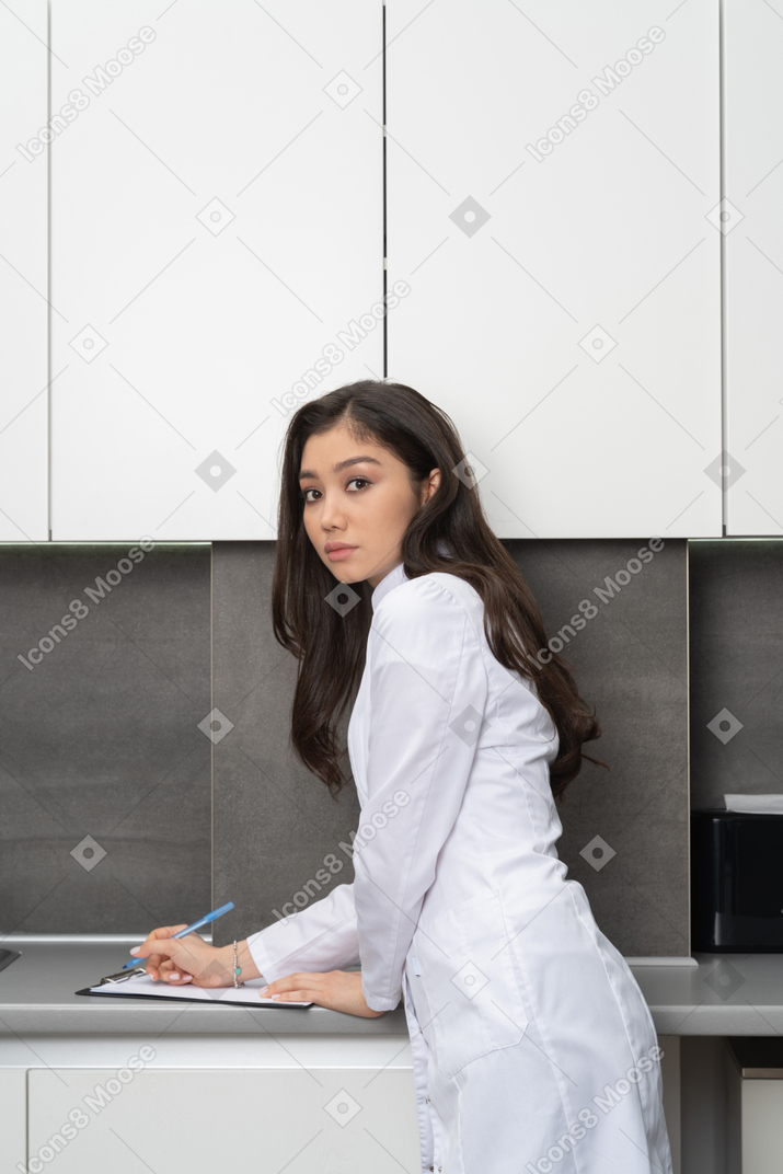Side view of a female doctor taking notes on her tablet and looking at camera