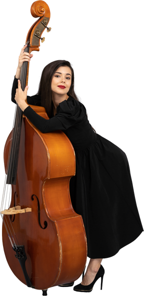 Vue de trois quarts d'une jeune femme musicienne en robe noire tenant sa contrebasse se penchant en avant