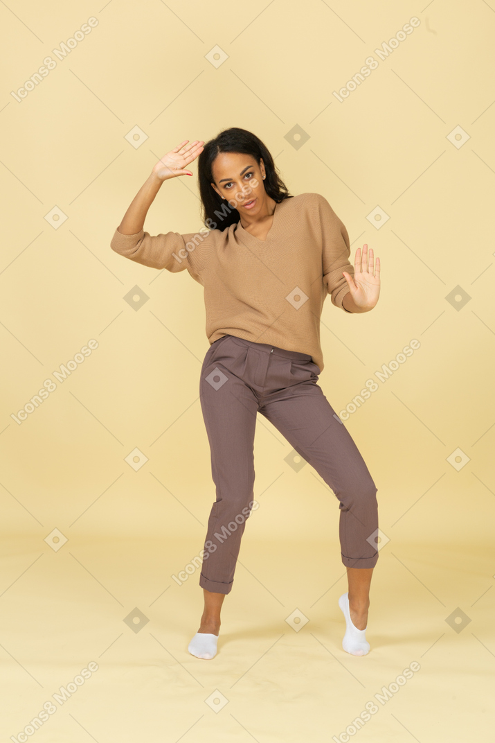 Vista frontal de una mujer joven bailando de piel oscura levantando la mano mientras mira a la cámara
