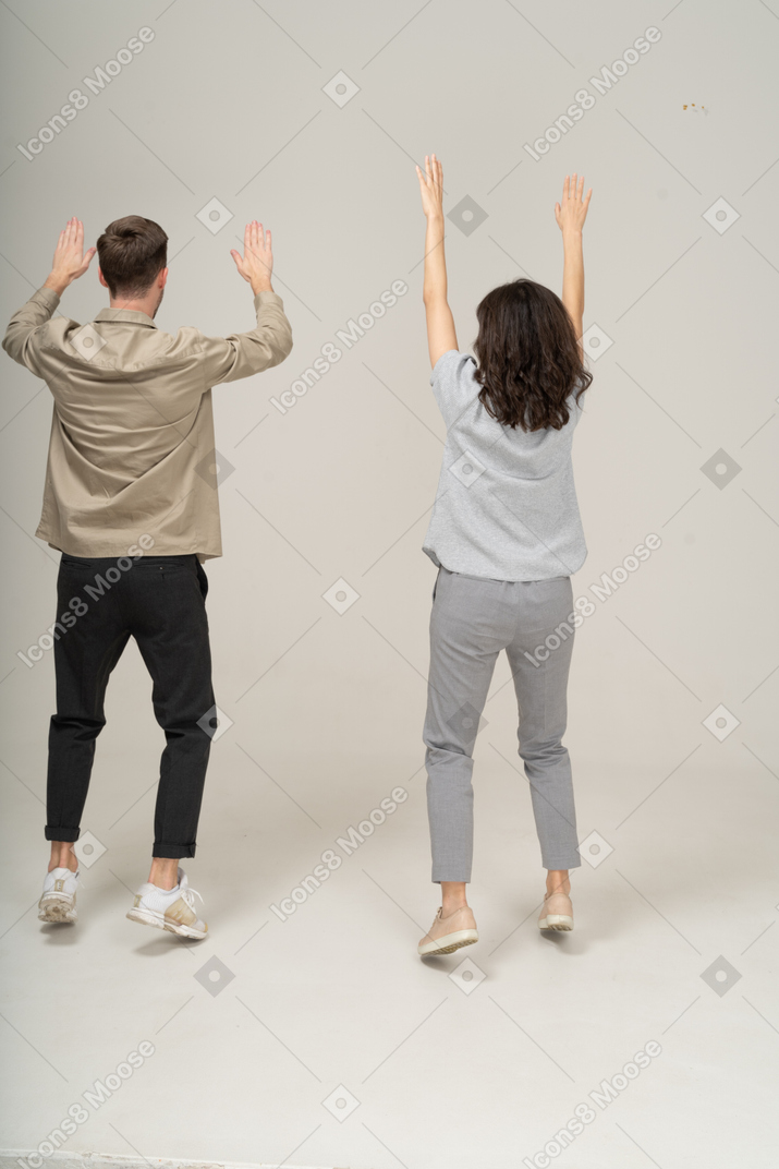 Vista traseira do jovem e da mulher com as mãos levantadas