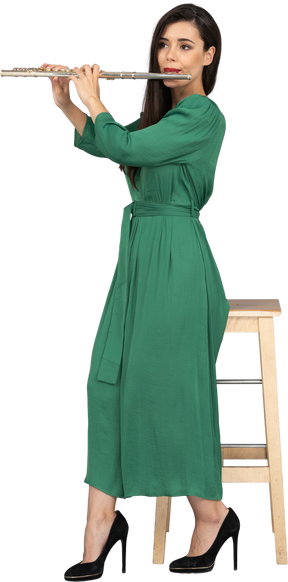 Vista lateral de uma jovem de vestido verde sentada em uma cadeira enquanto toca clarinete