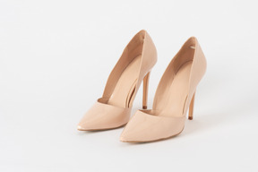 A three-quarter front shot of a pair of beige lacquered stiletto shoes