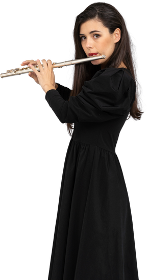 Vista lateral de uma jovem séria de vestido preto tocando flauta