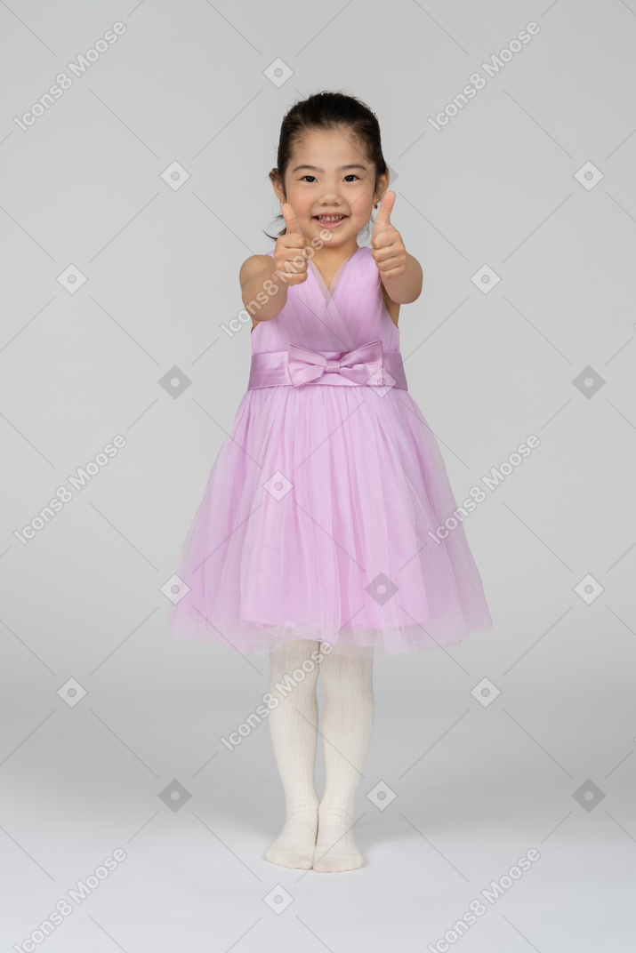 Full length photo of a little girl in a dress giving thumbs up