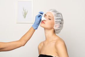 鼻形成術後の女性の鼻をテーピングする医師