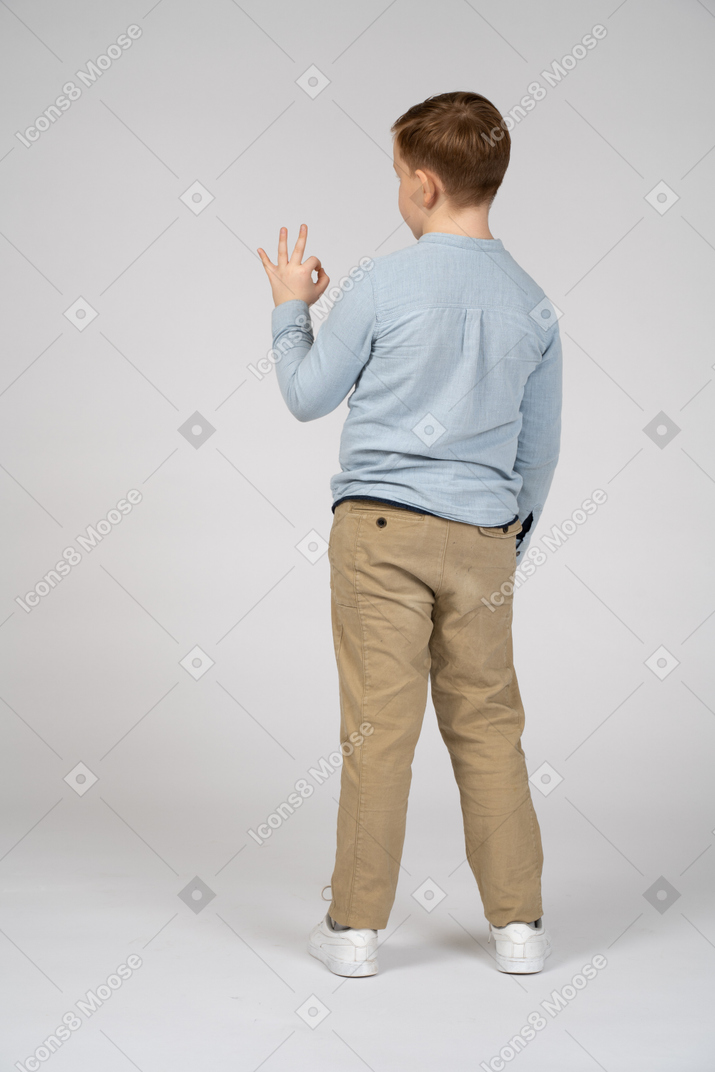 Vista traseira de um menino mostrando sinal de ok