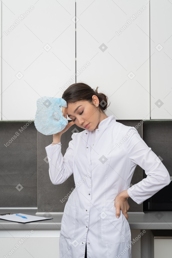 Front view of tired female doctor looking down and touching head