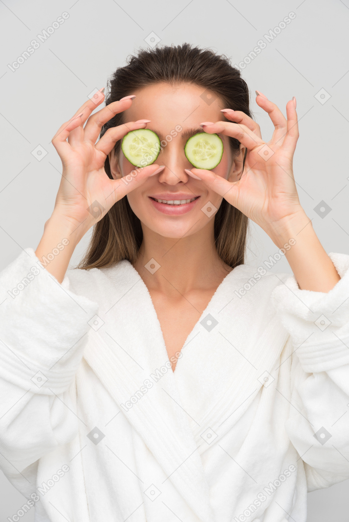 Beautiful young woman holding cucumber slices against her eyes