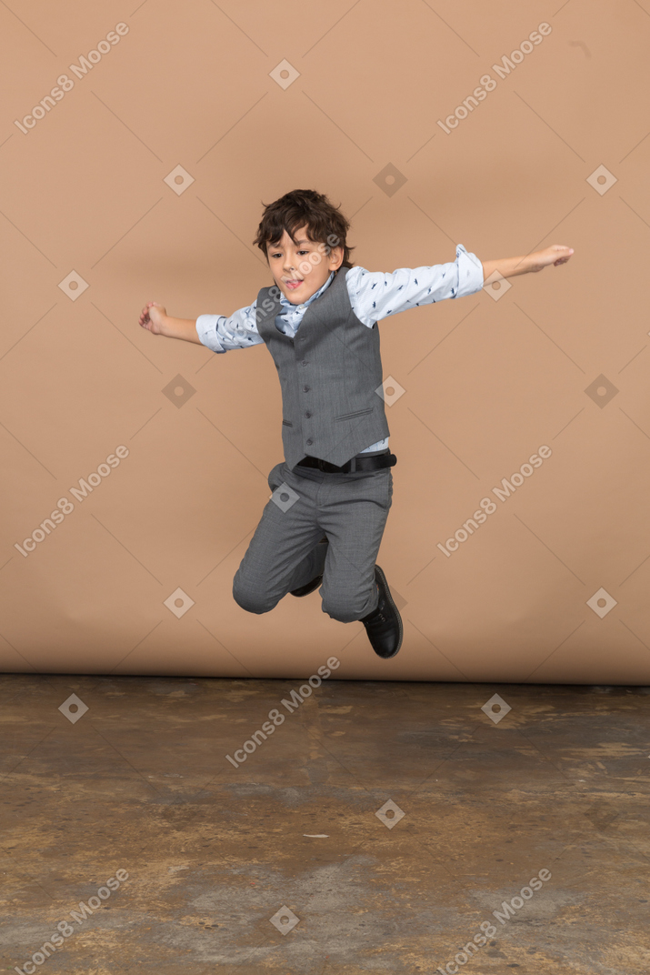 Front view of a cute boy in suit jumping with outstretched arms