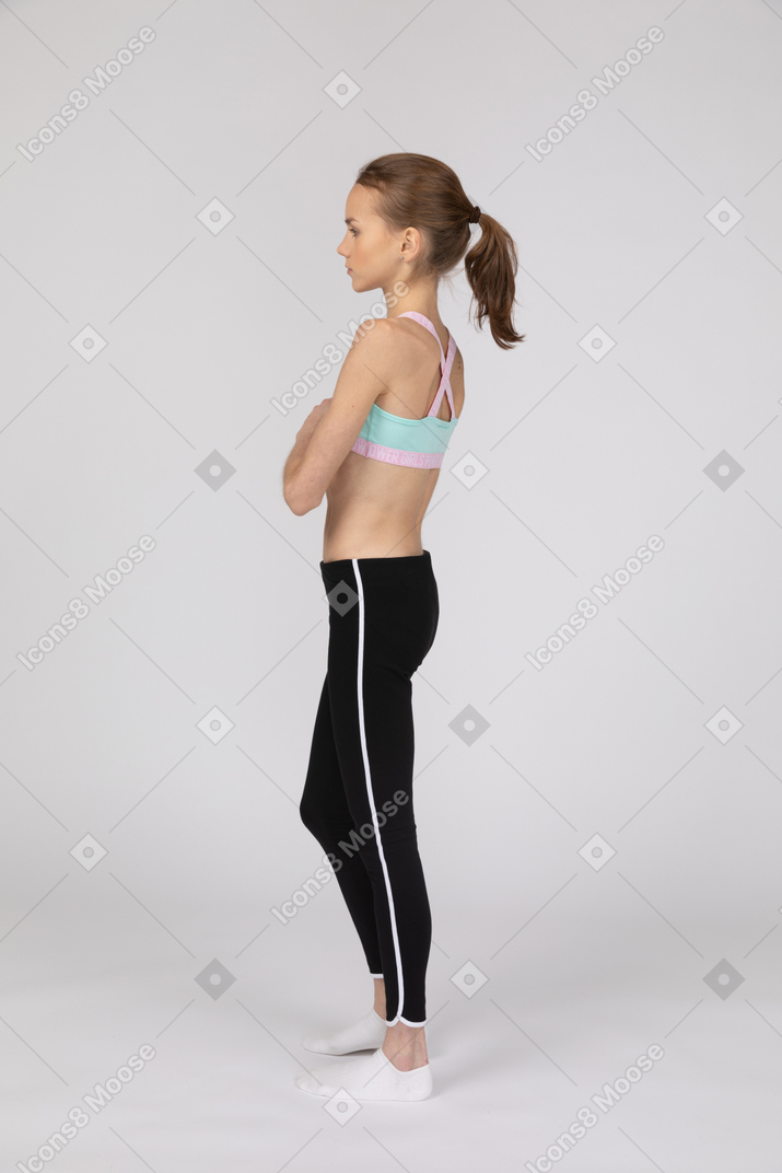 一个十几岁的女孩在运动服站着不动的侧视图