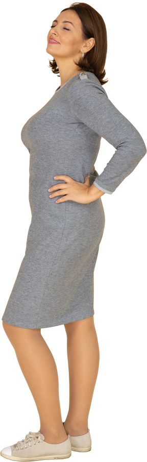 Side view of a woman in grey dress posing with hand on hip