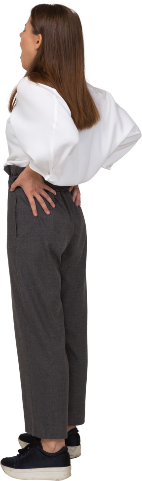 Vista posteriore di tre quarti di una giovane donna che sbadiglia in abiti da ufficio che mette le mani sui fianchi