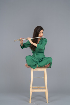 Full-length of a young lady playing the clarinet sitting with her legs crossed on a wooden chair