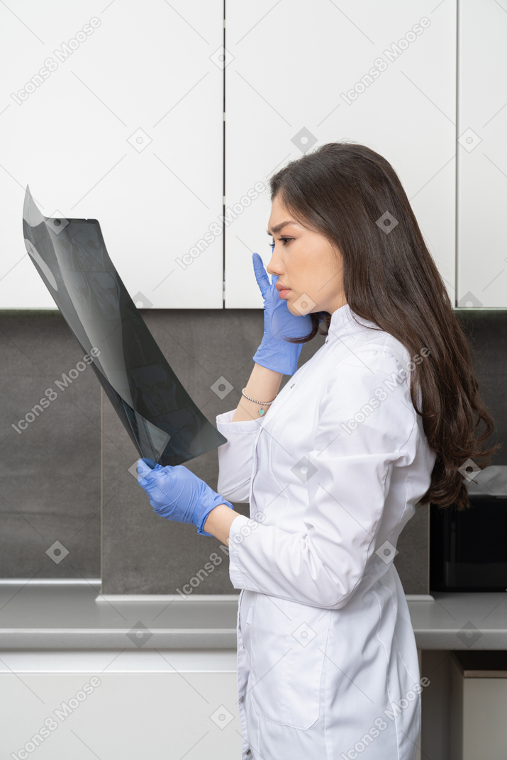 Vista lateral de uma jovem médica olhando para uma imagem de raio-x e tocando sua cabeça