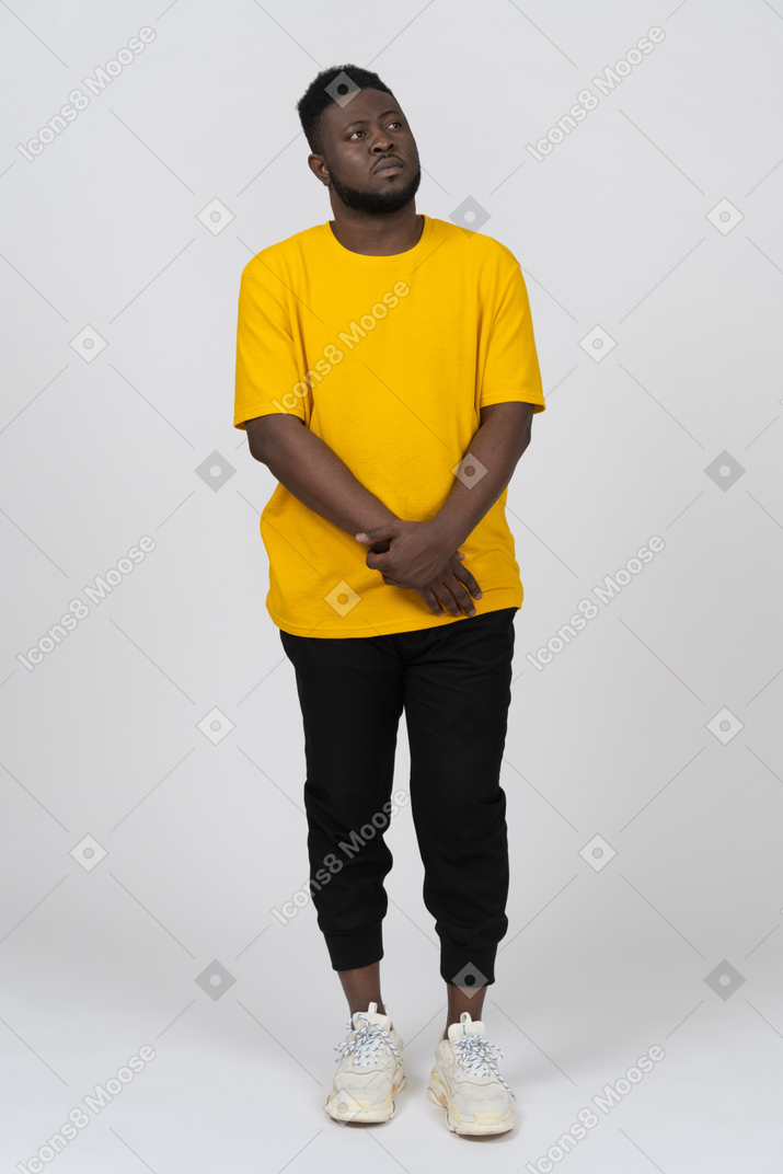 Front view of a shy young dark-skinned man in yellow t-shirt holding hands together