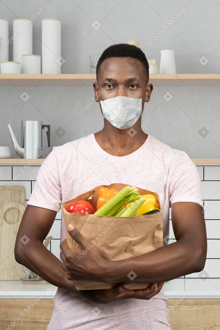 A man wearing a face mask holding a bag of vegetables