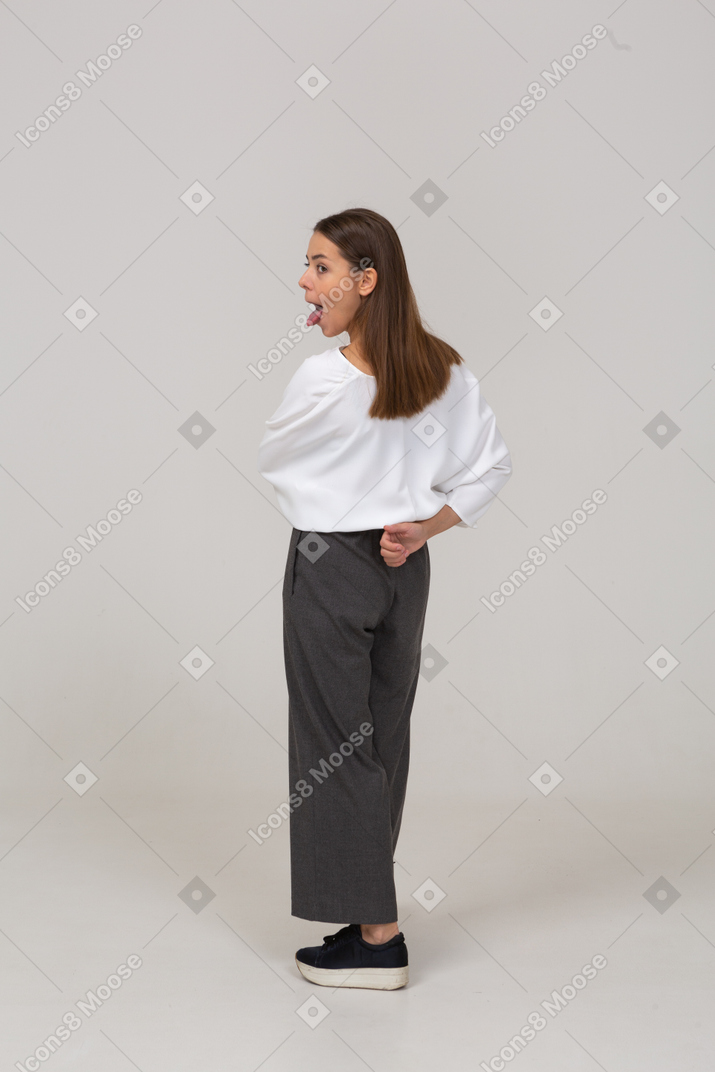 Вид сзади на три четверти молодой леди в офисной одежде, показывающей язык и держащейся за руку