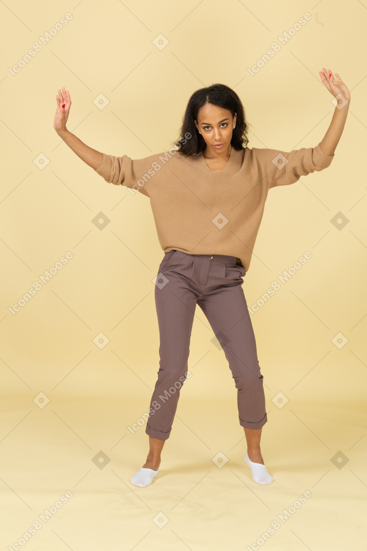 Vista frontal de una mujer joven bailando de piel oscura levantando las manos mientras mira a la cámara