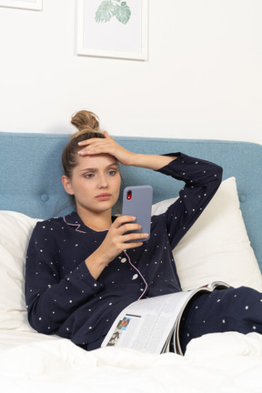 Close-up de uma jovem fêmea de pijama deitada na cama enquanto navega na internet