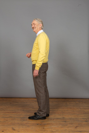 Vista lateral de um velho sorridente de pulôver amarelo levantando a mão e olhando para o lado