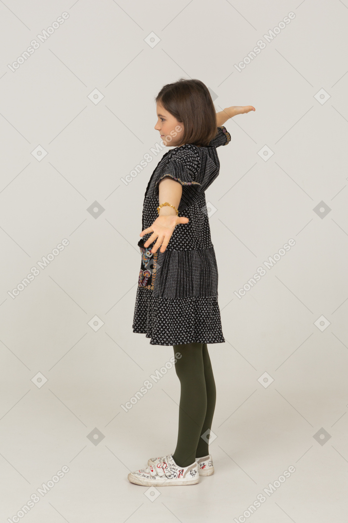 Vista laterale di una bambina in abito che allarga le braccia