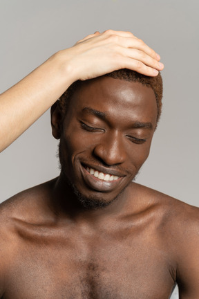 Main blanche touchant les cheveux d'un jeune homme noir