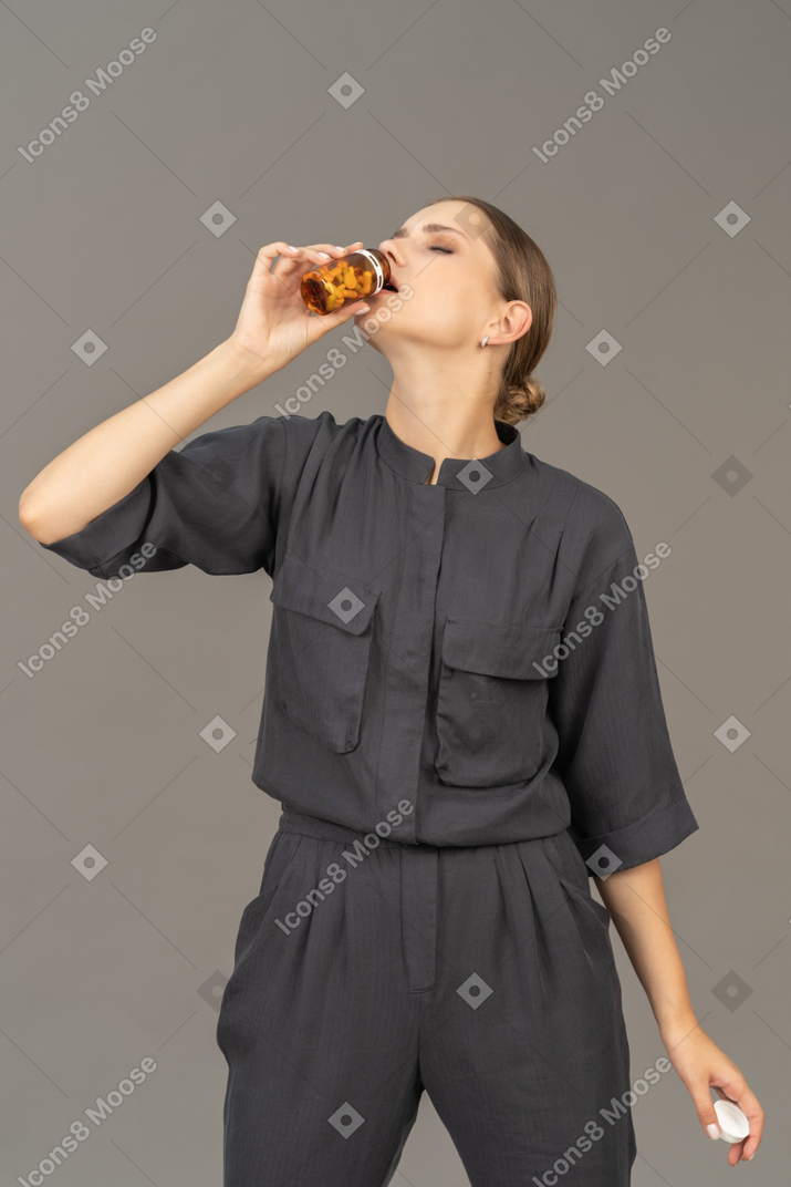 Vista frontal de uma jovem com um macacão tirando comprimidos de um frasco