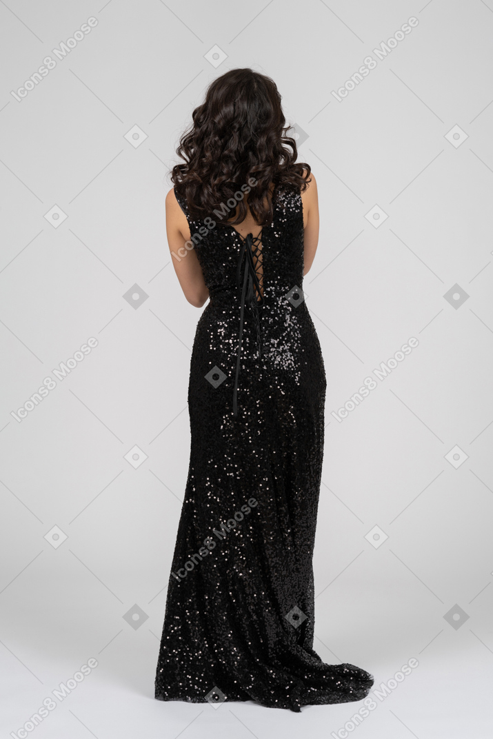 Женщина в черном вечернем платье стоит спиной к камере