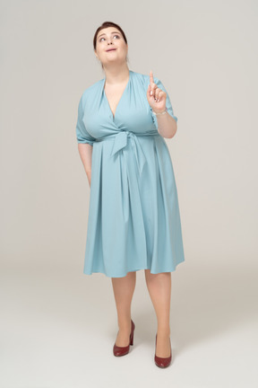 Vista frontal de una mujer en vestido azul apuntando hacia arriba con un dedo