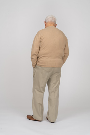 一位身穿休闲服、双手插在口袋里站着的老人的后视图