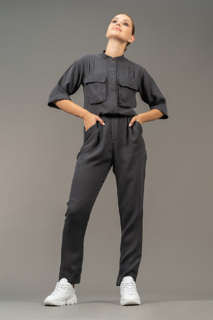 Front view of a proud young woman in a jumpsuit putting hands on hips