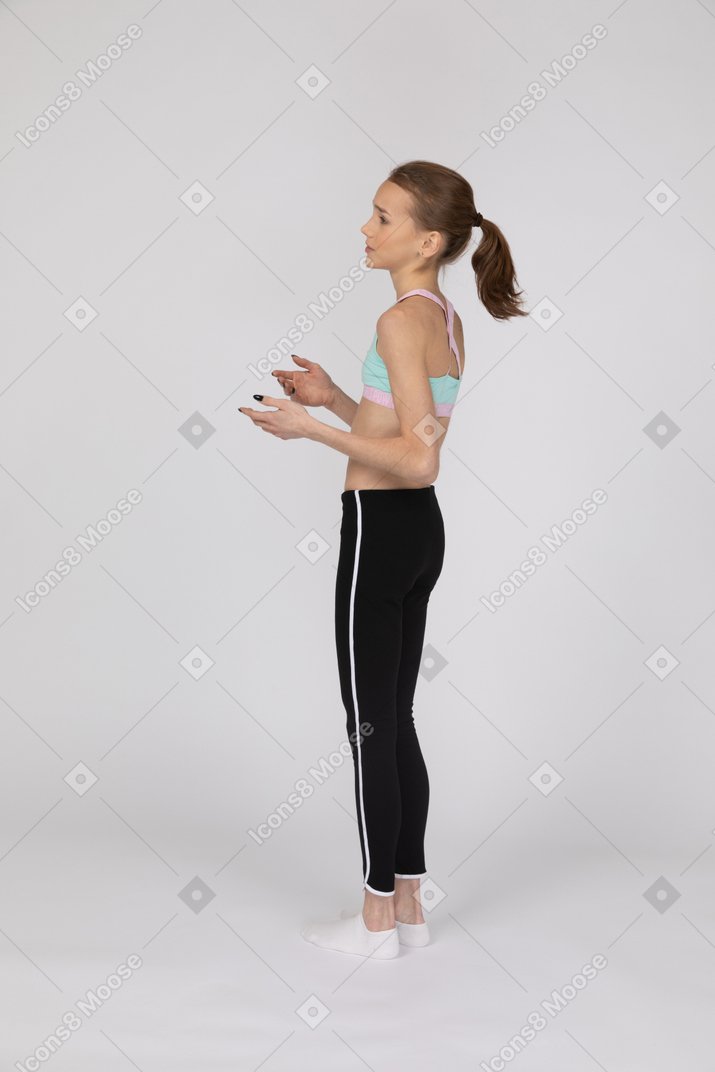 Side view of a teen girl in sportswear explaining something while raising hands