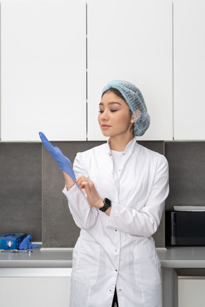 Vista frontal de una joven doctora poniéndose guantes protectores en su gabinete médico