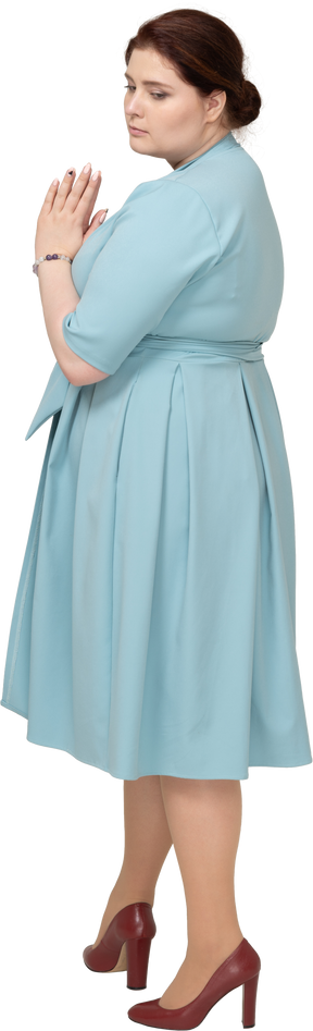 祈りのジェスチャーを作る青いドレスを着た女性の側面図