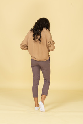 Three-back back view of a dark-skinned young female zipping up her pants