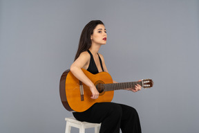 Three-quarter view of a sitting young lady in black suit holding the guitar