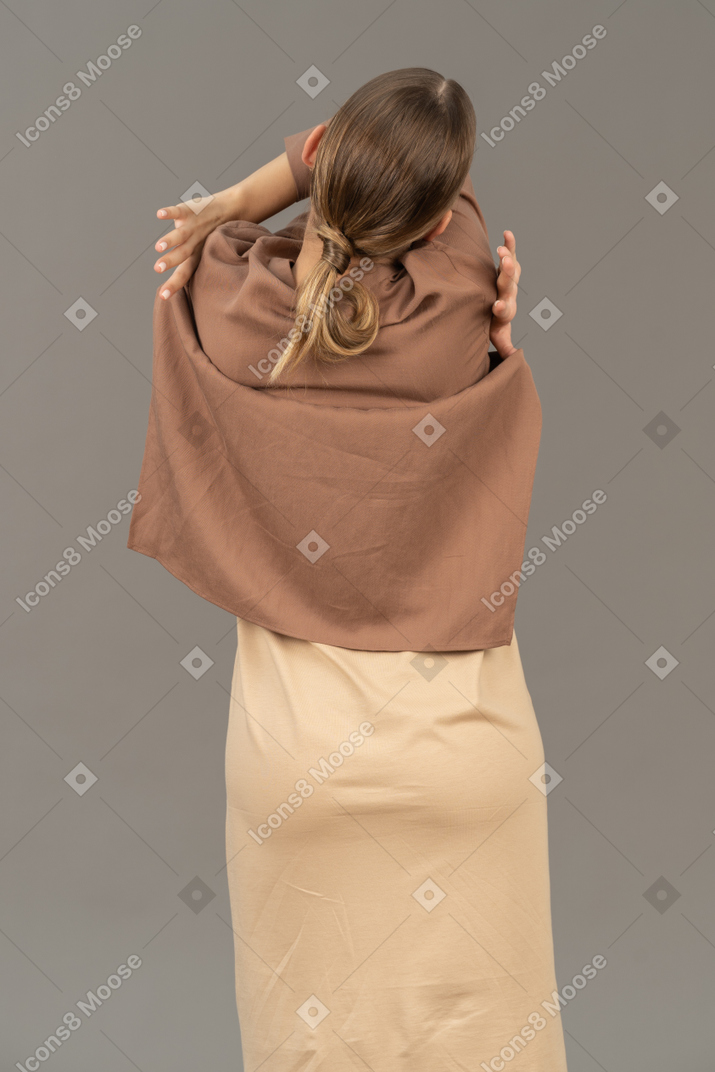Back view of a woman pulling off her shirt with crossed arms