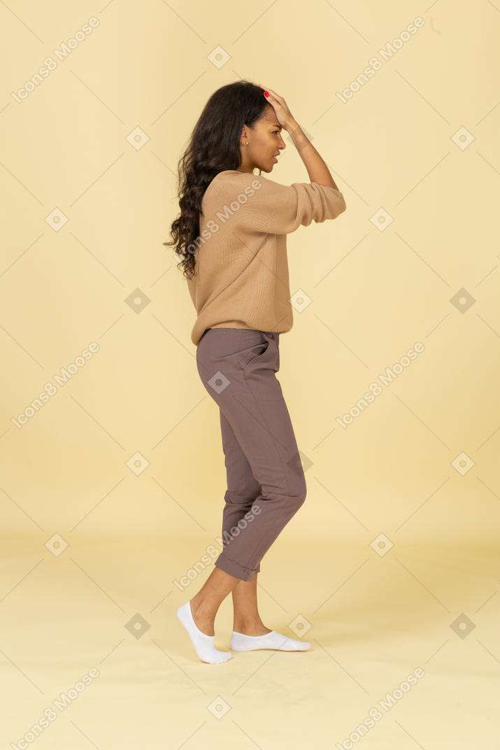 Vista lateral de una mujer joven de piel oscura tocando la frente
