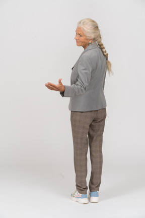 歓迎のジェスチャーをしているスーツの老婦人の背面図