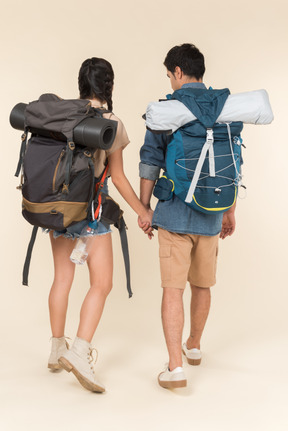 Young woman and man with backpacks holding hands