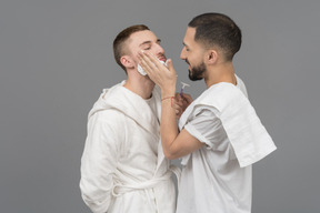 Jovem homem caucasiano aplicando espuma de barbear na bochecha do outro com um sorriso