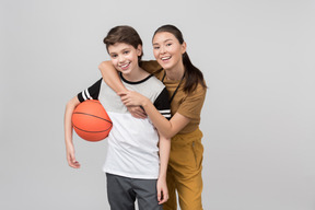Pe female teacher hugging her pupil which is holding basketball ball