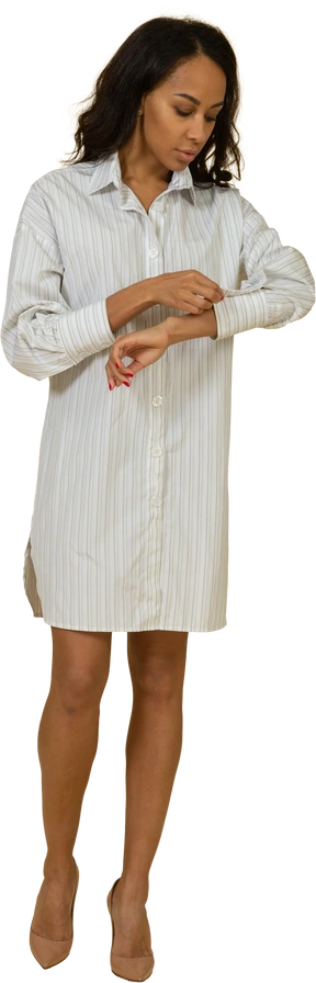 Front view of a dark-skinned young female in white dress buttoning up her sleeve