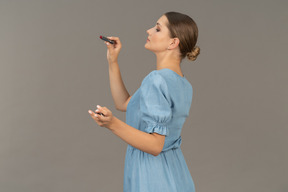 Vista lateral de uma jovem de vestido azul segurando um batom