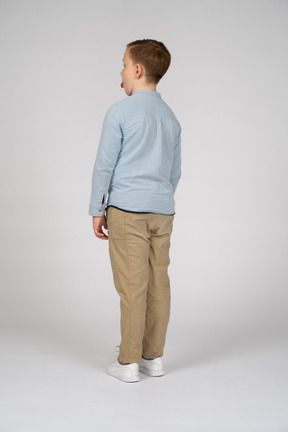 Вид сзади мальчика в повседневной одежде, показывающего язык