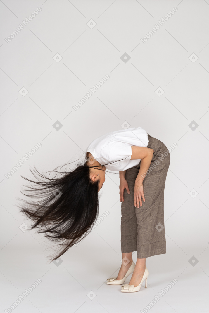 一位年轻的女士，穿着马裤和t恤，凌乱的头发弯下腰，四分之三的视图