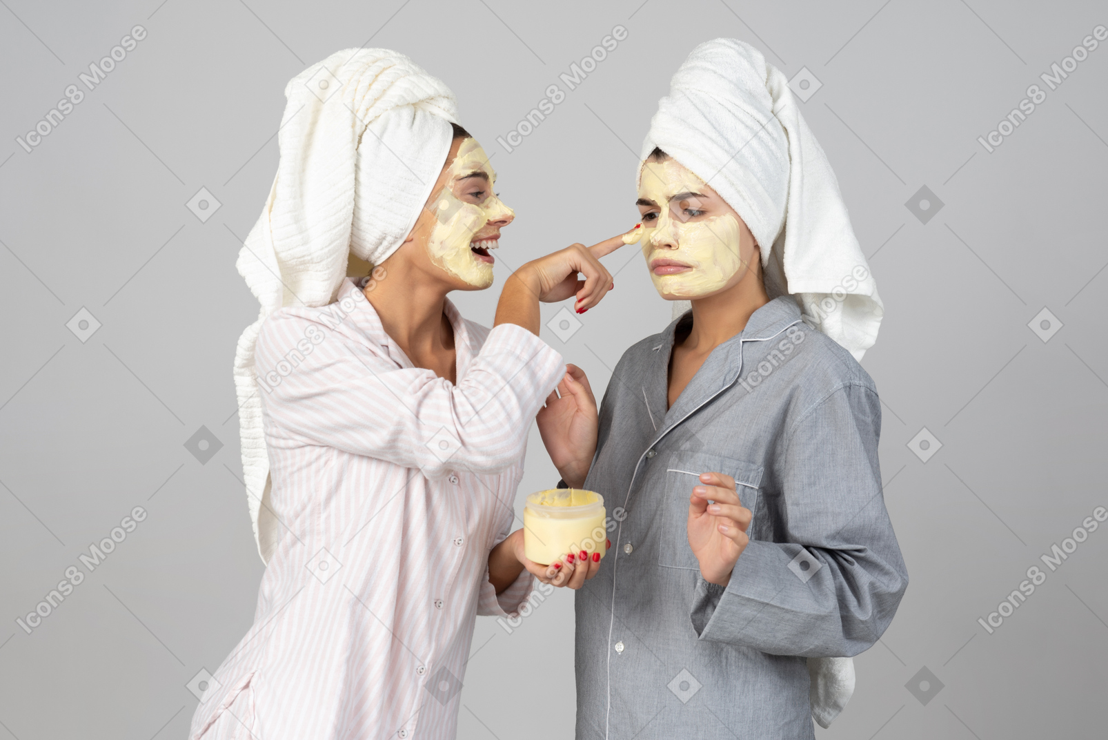 Two young girls with hair wrapped in towels applying creme masks on face