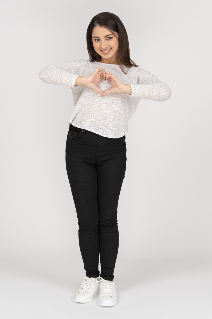 Front view of a young indian female in casual clothing showing heart gesture