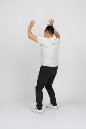 Вид сзади на человека в повседневной одежде, стоящего с поднятыми руками