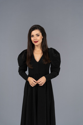 Vista frontale di una giovane donna sorridente in un abito nero in piedi ancora